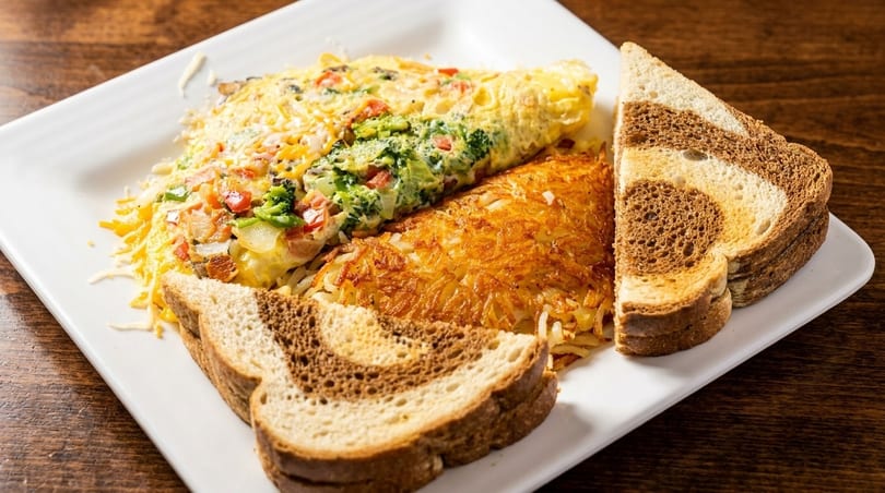 A breakfast plate with a vegetable omelet, crispy hash browns, and marbled rye toast.